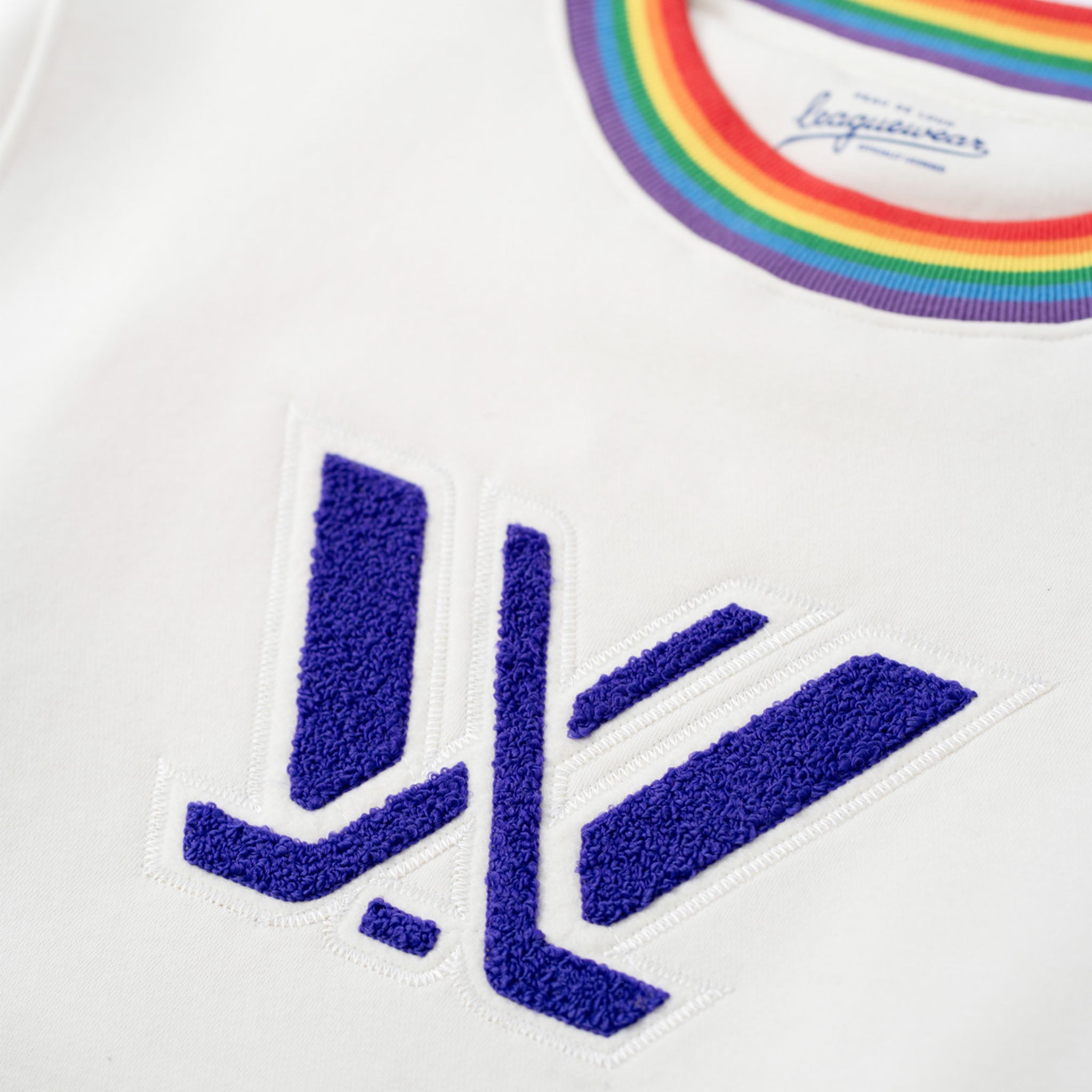 White shirt with blue logo and rainbow collar, featuring a brand name.