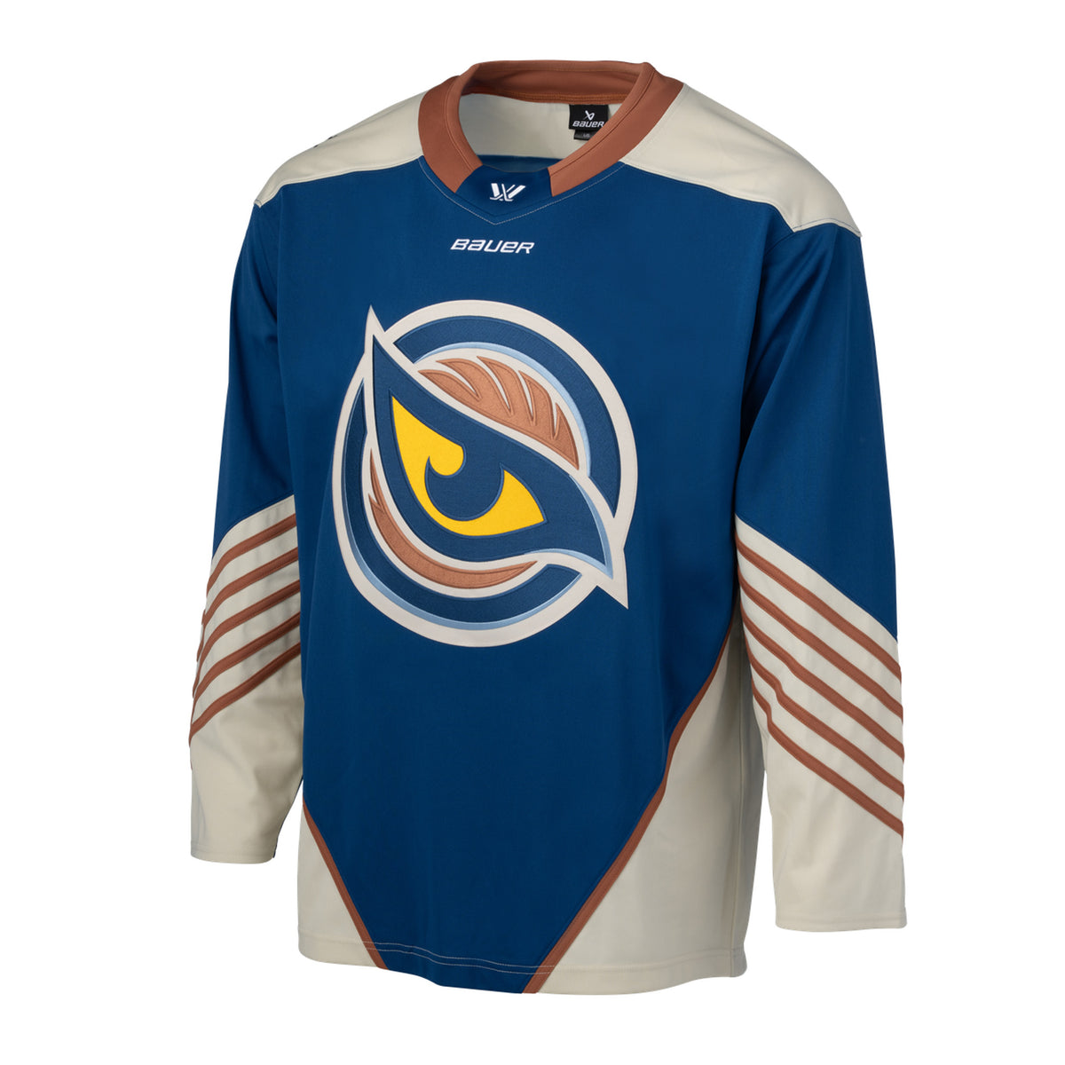 Front of a blue jersey with the Vancouver Goldeneyes logo in the center. The hips have cream color blocking with a tan line on top. The tan collar has a blue color block with the PWHL logo and the Bauer logo is beneath it. The cream shoulder caps have the PWHL logo on the left shoulder. From the elbow down is cream with small tan stripes.