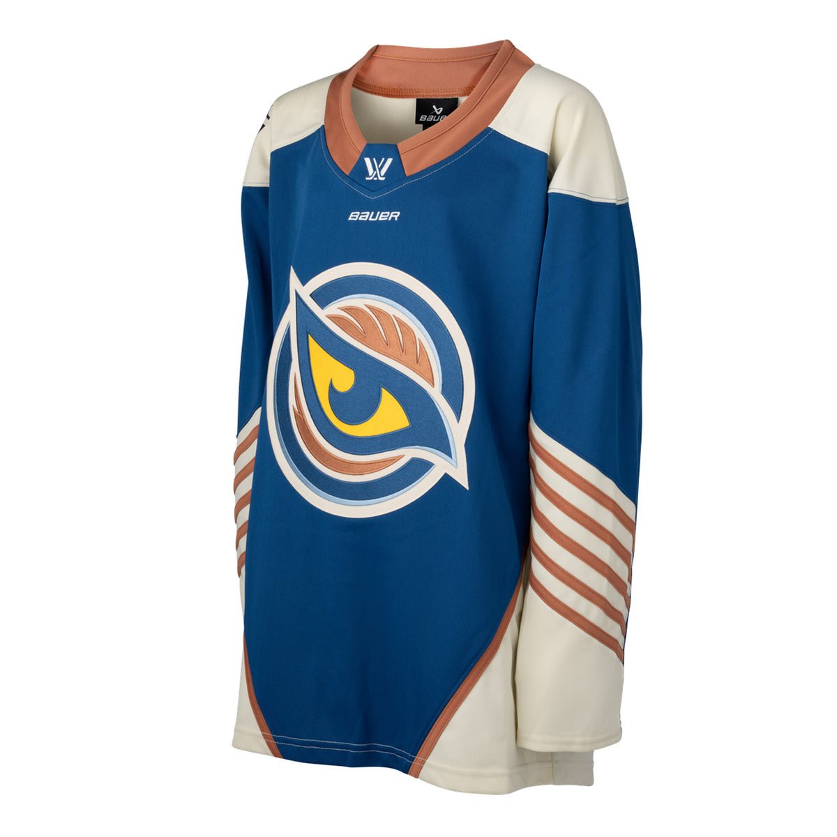 Front of a blue jersey with the Vancouver Goldeneyes logo in the center. The hips have cream color blocking with a tan line on top. The tan collar has a blue color block with the PWHL logo and the Bauer logo is beneath it. The cream shoulder caps have the PWHL logo on the left shoulder. From the elbow down is cream with small tan stripes.