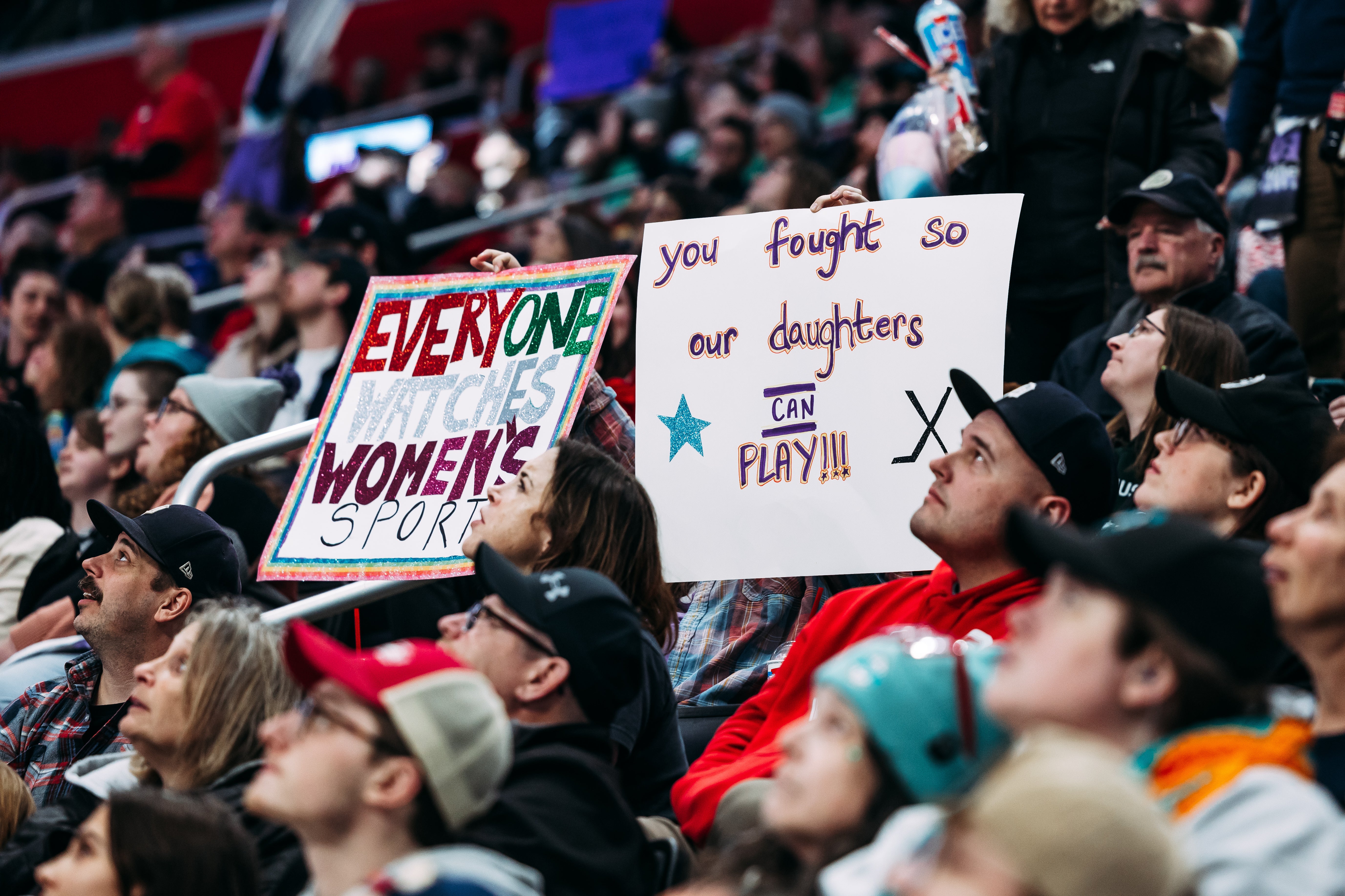Audience at a sports event holding signs supporting women's sports.