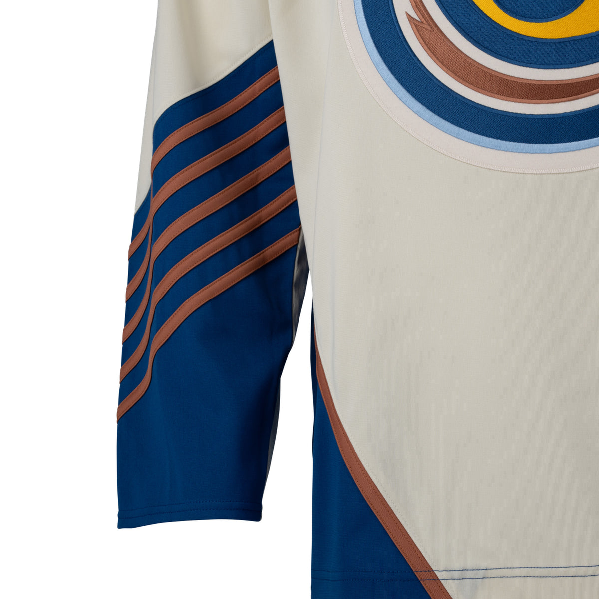 Front of a cream-colored jersey with blue color blocking on the hips with a tan line on top. The sleeves are cream and from the elbow down are blue with small tan stripes. 