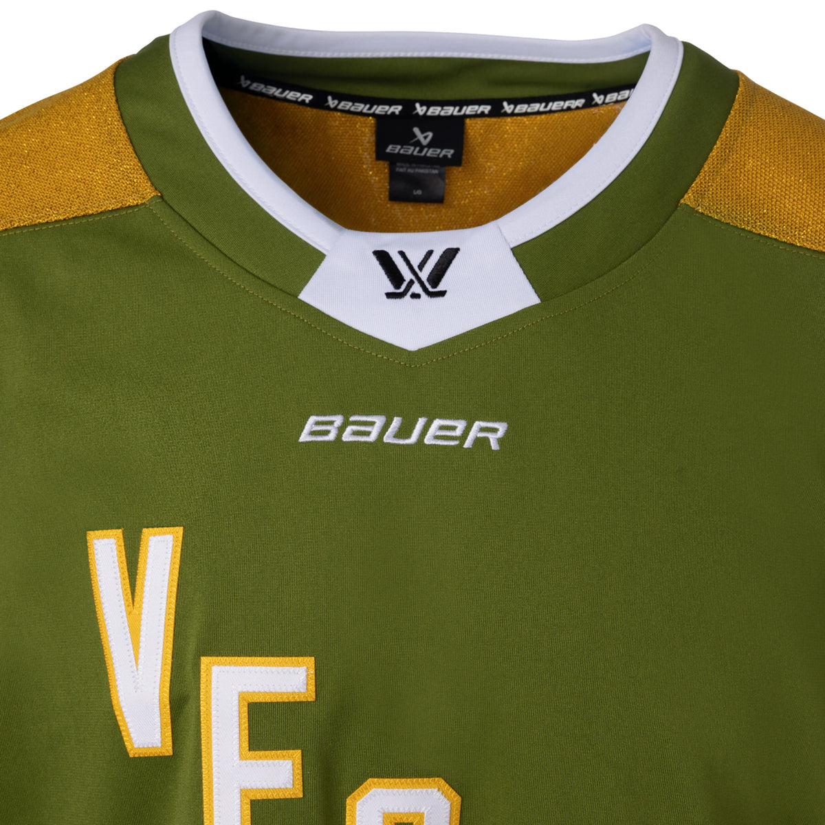 Front of a green jersey with sparkling gold shoulder caps and stripes along the sleeves surrounded by white and black stripes. In white outlined in gold reads 'VEGAS' diagonally across the chest. The collar is green with white trim on top. A black PWHL logo is centered on the collar with a white BAUER logo below it. 