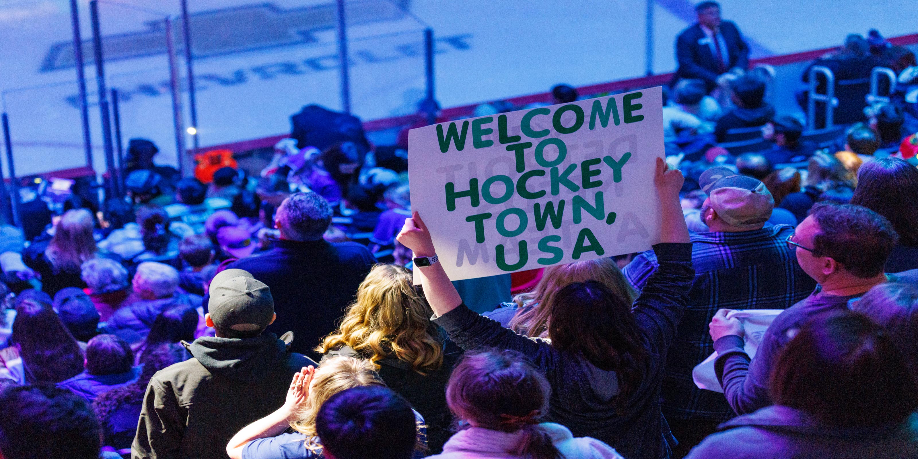 Person holding a 'Welcome to Hockey Town, USA' sign at a hockey game.