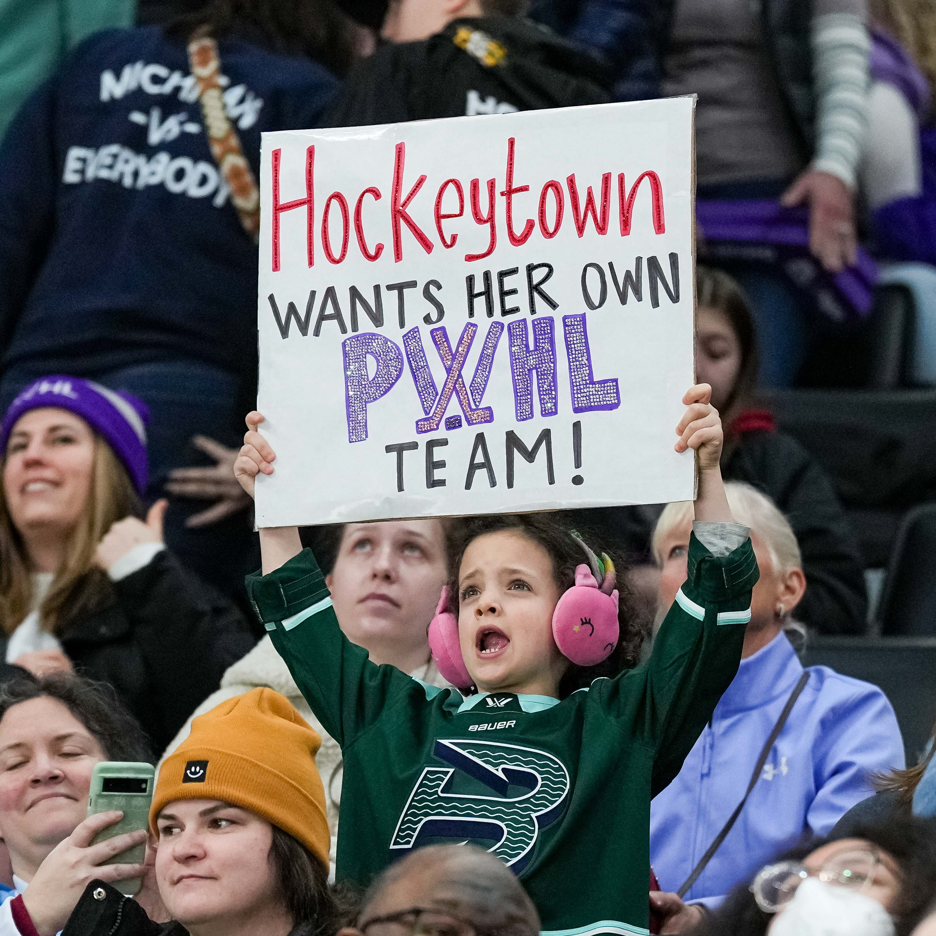 Child holding a sign in a crowd with text 'Hockeytown wants her own Pixie Lottle team!'