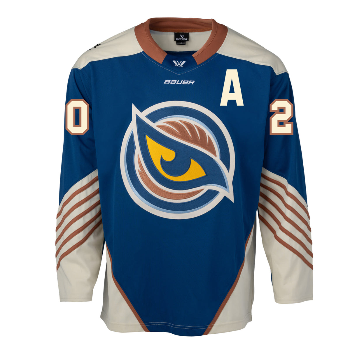Front of a blue jersey with the Vancouver Goldeneyes logo in the center and a cream 'A' on the left chest. The hips have cream color blocking with a tan line on top. The tan collar has a blue color block with the PWHL logo and the Bauer logo is beneath it. The cream shoulder caps have the PWHL logo on the left shoulder. The number '20' on the sleeves are cream with tan outlining. From the elbow down is cream with small tan stripes.